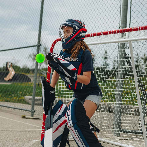 A young goalie in gear catching a green ball while playing with Road Warrior Street Hockey Balls - 15 Pack (Extreme Colours)