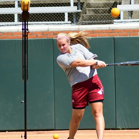 Athlete using Louisville Slugger soft-toss system for batting practice with softballs in motion